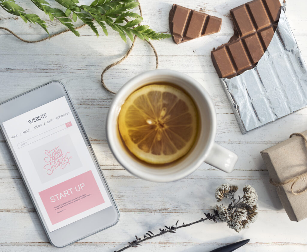 Pause gourmande et réconfortante avec une infusion fruitée au citron, du chocolat et un smartphone sur une table en bois blanc.
