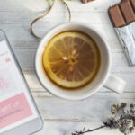 Pause gourmande et réconfortante avec une infusion fruitée au citron, du chocolat et un smartphone sur une table en bois blanc.
