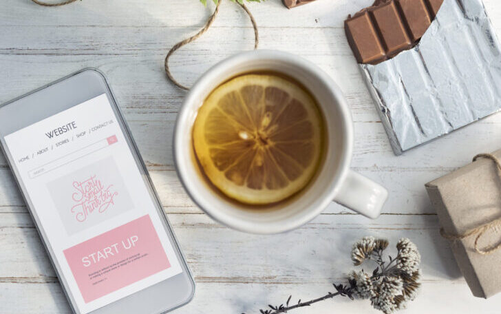 Pause gourmande et réconfortante avec une infusion fruitée au citron, du chocolat et un smartphone sur une table en bois blanc.